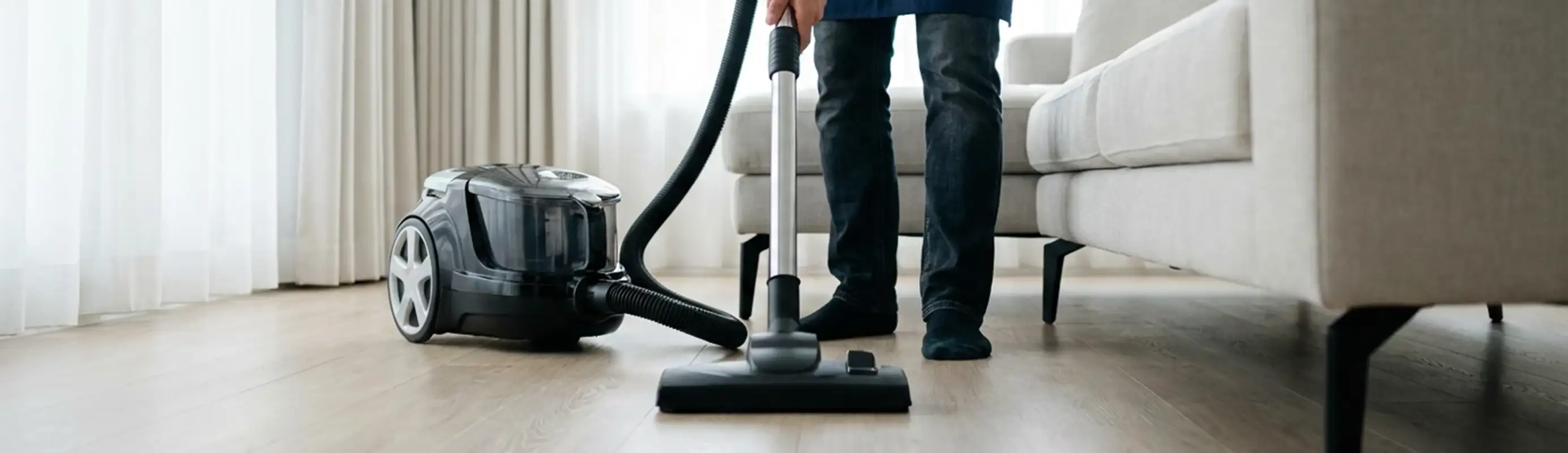 Professional house cleaner vacuuming a living room floor with a canister vacuum cleaner, Orlando, FL.