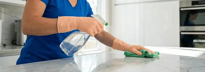 Maid service worker spraying and wiping a kitchen countertop with a microfiber cloth for sanitizing, Orlando, FL.