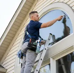 Professional window cleaner on a ladder using a squeegee to clean an exterior arched window, Orlando, FL.