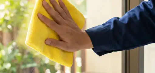 House cleaner wiping a glass window with a yellow microfiber cloth for streak-free cleaning, Orlando, FL.